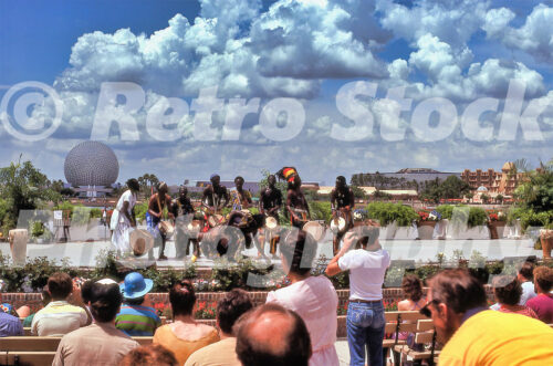 Alt Text A 1980s color photo of a live African drumming and dance performance on the World Showcase promenade at Epcot Center in Florida, with Spaceship Earth and the Mexico pavilion visible across the lagoon.
