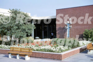 A 1960s color photo of the Fountain of Noah sculpture at Northland Center in Southfield, Michigan, featuring red and white flowers, brick planters, and wooden benches.