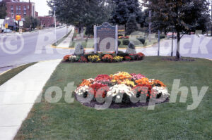 A 1970s colour photo of a Michigan Historical Marker for German Settlers in Frankenmuth, featuring vibrant flower beds and a street view with a Shell gas station sign.