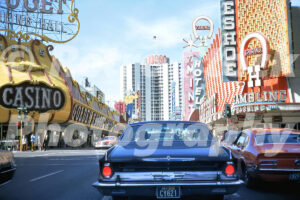 A 1970s color photo taken from behind a dark sedan looking down Fremont Street toward the Plaza Hotel, flanked by the Golden Nugget and Binion's Horseshoe in 1972.