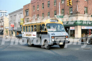 A 1970s color photo of a yellow and silver Mass Transportation Authority bus at the corner of Harrison and E 2nd Street in Flint, Michigan, with Drew's Stride Rite Shoes in the background.