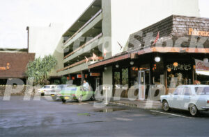 A 1970s colour photo of the Hilo Bay Hotel in Hawaii, featuring a green Ford Pinto in the parking lot, a Polynesian-style shingle roof, and a Sundries shop.