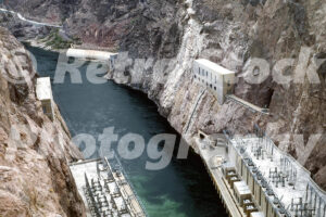 A 1960s colour photo of the rugged canyon walls, the deep blue Colorado River, and the Hoover Dam power plant in 1960s.