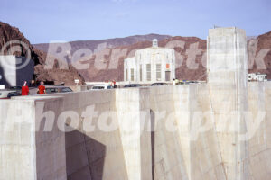 A 1970s colour photo of the massive concrete dam wall, the Nevada intake tower, and vintage cars at Hoover Dam in 1970s.
