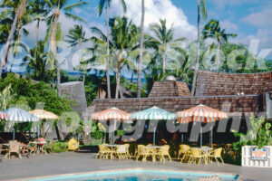 A 1970s colour photo of the Hotel Molokai in Hawaii, featuring a swimming pool, striped patio umbrellas, and A-frame Polynesian-style bungalows under palm trees.