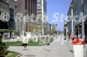 A 1960s color photo of the Kalamazoo Mall in Michigan, featuring wide pedestrian walkways, a white statue on a green lawn with pink tulips, and historic bank buildings.