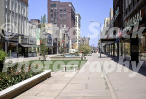A 1960s color photo of the Kalamazoo Mall in Michigan, featuring a wide pedestrian walkway with concrete benches, a small bridge over a water feature, and a Walgreens storefront.