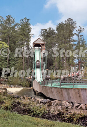 A 1970s color photo of the Shenandoah Lumber Company log flume at Kings Dominion in Virginia, featuring a log boat carrying passengers down a steep turquoise chute into a splashdown pool surrounded by pine trees.