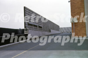 A 1960s color photo of the "Delivery Trucks Only" ramp at Lloyd Center in Portland, Oregon, featuring a tall textured concrete wall and a red brick building.
