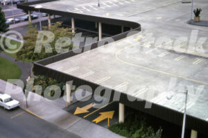 A 1960s color photo taken from the Sheraton Hotel looking down at the multi-level parking structure at Lloyd Center in Portland, Oregon, featuring yellow directional arrows and mid-century modern design.
