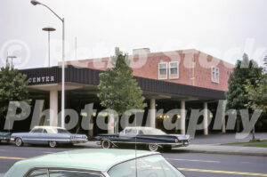 A 1960s color photo of the Lloyd Center in Portland, Oregon, featuring the Meier & Frank department store building and a dark blue vintage Buick convertible parked on the street.