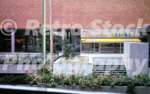 A 1960s color photo of the Van Duyn Candies storefront and a sunken garden featuring a small fountain and rose bushes at Lloyd Center in Portland, Oregon.