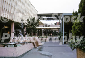 A 1960s color photo of a tiered modern metal fountain in a concrete basin at Lloyd Center in Portland, Oregon, set against a geometric textured building facade and open-air walkways.