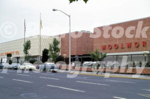 A 1960s color photo of the J.C. Penney Co. and Woolworth storefronts at Lloyd Center in Portland, Oregon, featuring brick architecture and vintage cars parked along the street.