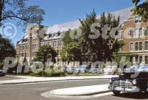 A 1950s color photo of Landon Hall at Michigan State University in East Lansing, featuring Collegiate Gothic brick architecture and a parking lot filled with vintage 1950s cars.