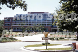 A 1950s color photo of the Student Services Building at Michigan State University in East Lansing, featuring mid-century brick and glass architecture with a Yield Right of Way sign in the foreground.