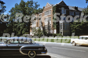 A 1950s color photo of Landon Hall at Michigan State University in East Lansing, featuring its red brick Collegiate Gothic architecture and vintage cars parked in the foreground.