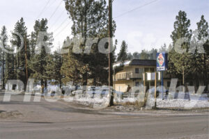 A 1980s color photo of a Motel 6 in Big Bear Lake, California, featuring a two-story beige building, a blue vintage sign, and patches of snow on the ground surrounded by pine trees.