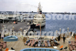 A 1960s color photo taken from the deck of the Cunard liner Franconia at Port Everglades, Florida, showing passengers in deck chairs and the ship Ariadne docked nearby in the harbor.