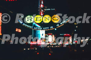 A 1980s color photo of the glowing yellow and blue Reno Arch and the neon signs of Harolds Club and the Riverside in Reno in 1980s.
