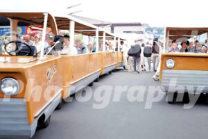 A 1960s color photo of yellow Fairliner trams carrying passengers at the Seattle World's Fair in Washington, with fairgoers in vintage attire walking alongside the vehicles.