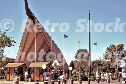 A 1970s color photo of the main entrance to SeaWorld San Diego in California, featuring a massive Polynesian-style A-frame structure and colorful flags under a clear blue sky.