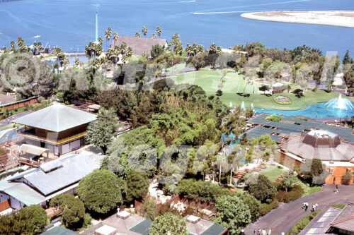 A 1970s color photo of the SeaWorld San Diego landscape in California, featuring the Japanese Village, a calm lagoon with fountains, and the tall blue Skytower needle in the distance overlooking Mission Bay.