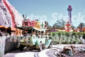 A 1960s color photo of the Fiesta Train ride at Six Flags Over Texas in Arlington, featuring a colorful character-filled bus vehicle on a track with a large pink volcano