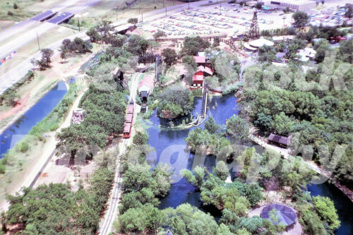 A 1960s color photo of an aerial view of Six Flags Over Texas in Arlington, featuring the Six Flags Railroad, the Log Flume, and the oil derrick Tower in the distance.