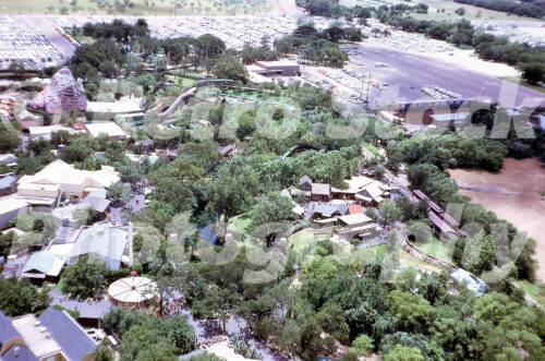 A 1960s color photo of an aerial view of Six Flags Over Texas in Arlington, featuring the sprawling park layout, the log flume, and the large parking lot filled with vintage cars.