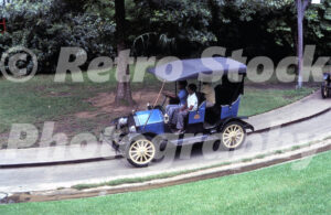 A 1970s color photo of the Chaparral Antique Cars ride at Six Flags Over Texas in Arlington, featuring three young guests driving a vintage-style blue motorcar on a guided track.