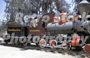 A 1960s color photo of a steam locomotive at Six Gun Territory in Silver Springs, Florida, featuring children waving from the "Southern Railway & Six Gun" engine cab amidst Spanish moss-draped trees.