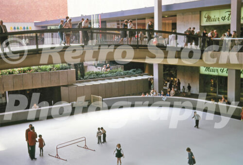 Skating rink at Lloyd Center, Portland OR 1963 A 1960s color photo of the open-air ice skating rink at Lloyd Center in Portland, Oregon, with spectators watching from a pedestrian bridge and the Meier & Frank storefront in the background.