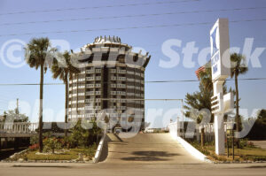A 1980s color photo of the Hilton Inn entrance in St. Petersburg, Florida, featuring a white pylon sign, a concrete access ramp, and the unique circular architecture of the St. Petersburg Beach Hilton in the background.