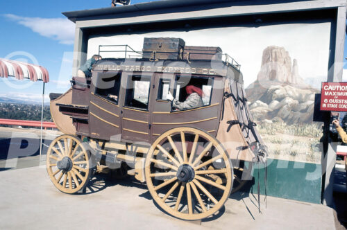 A 1970s color photo of a Wells Fargo Express Co. stagecoach prop at Universal Studios Hollywood, featuring a moving background screen depicting a desert landscape.