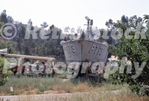 A 1970s color photo of the PT-73 boat from the television show McHale’s Navy, resting on wooden blocks in a grassy backlot area at Universal Studios Hollywood.