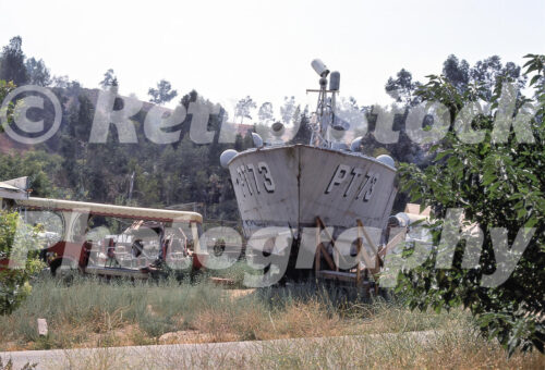 A 1970s color photo of the PT-73 boat from the television show McHale’s Navy, resting on wooden blocks in a grassy backlot area at Universal Studios Hollywood.