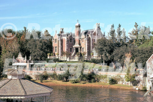 A 1970s color photo of the Haunted Mansion in Liberty Square at Walt Disney World, featuring the red-brick Hudson River Gothic manor and a gazebo in the foreground.