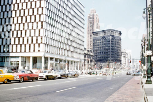 A 1960s color photo of vintage cars on Woodward Avenue with the white Qube building and the dark Majestic building in Detroit, Michigan in 1961.