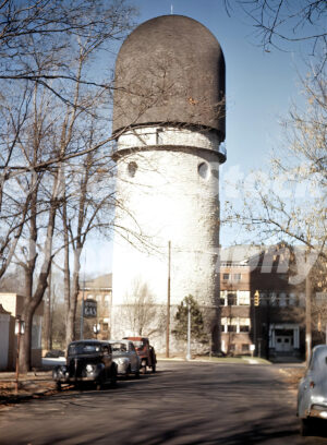 A 1940s color photo of the limestone Ypsilanti Water Tower in Michigan, featuring its distinctive dome-shaped roof and vintage cars parked along the street.
