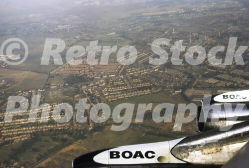 Vintage colour photo taken from a BOAC Boeing 707 in 1972, showing the jet engine and wing above suburban landscape below.