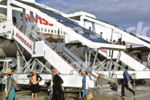 A 1980s color photo of passengers using Swissair mobile staircases to disembark from a plane at Geneva Airport in 1982.