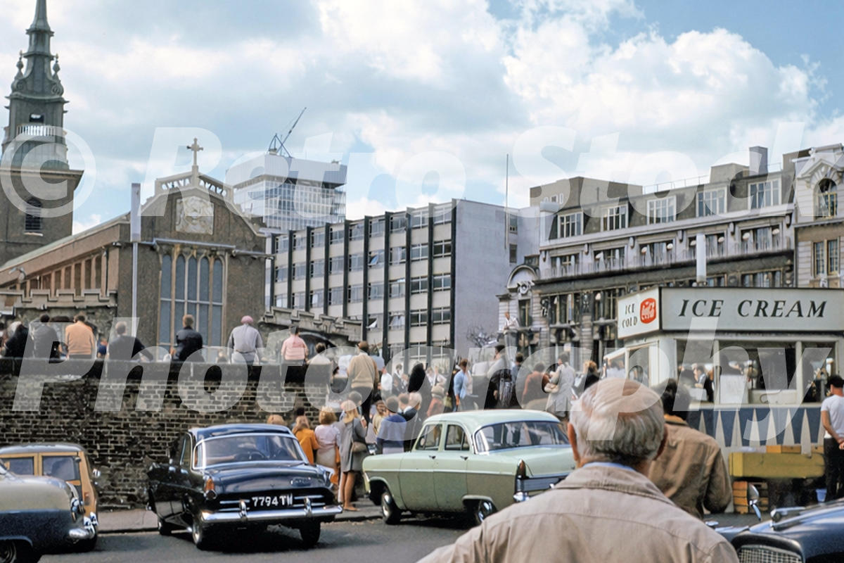 1960s photo of All Hallows-by-the-Tower in London, with crowds gathered outside, period cars, an ice-cream kiosk and modern office blocks behind.