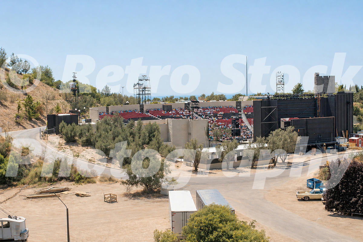1970s view of the outdoor Universal Amphitheatre at Universal Studios Hollywood, with red seating, stage structures and studio roads around it.