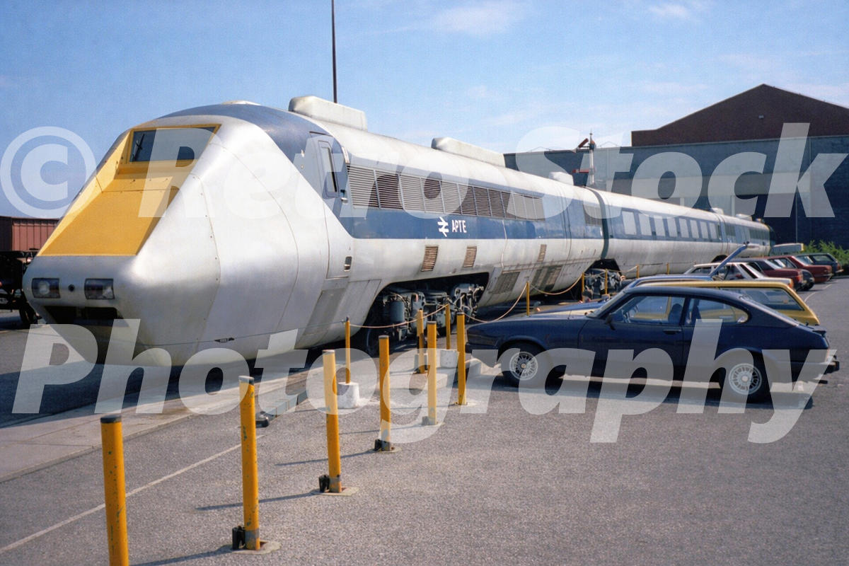 1980s photo of the APT-E at the National Railway Museum in York, with the streamlined prototype train displayed outdoors beside parked cars.