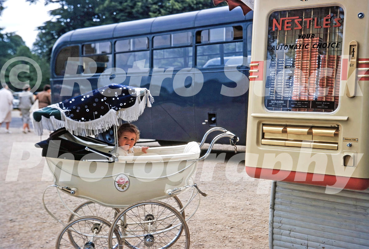 baby-and-vending-machine-london-1959_55231895643_o A 1950s colour photo of a young child in a vintage cream-coloured pram parked next to a Nestlé’s chocolate vending machine, with a blue bus in the background.