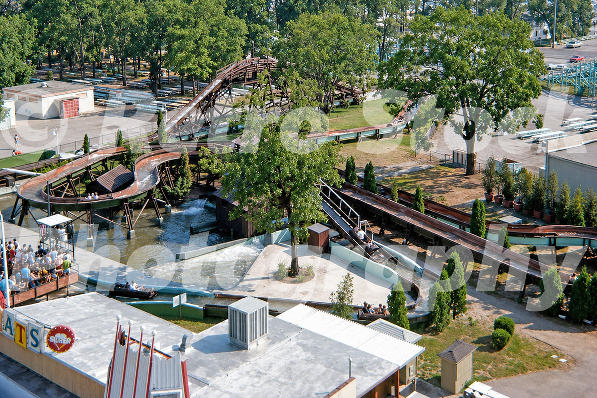 A 1970s color photo of the Mill Race log flume at Cedar Point in Sandusky, Ohio, featuring several log boats navigating a winding watercourse through trees, with the park museum and midway visible in the background.