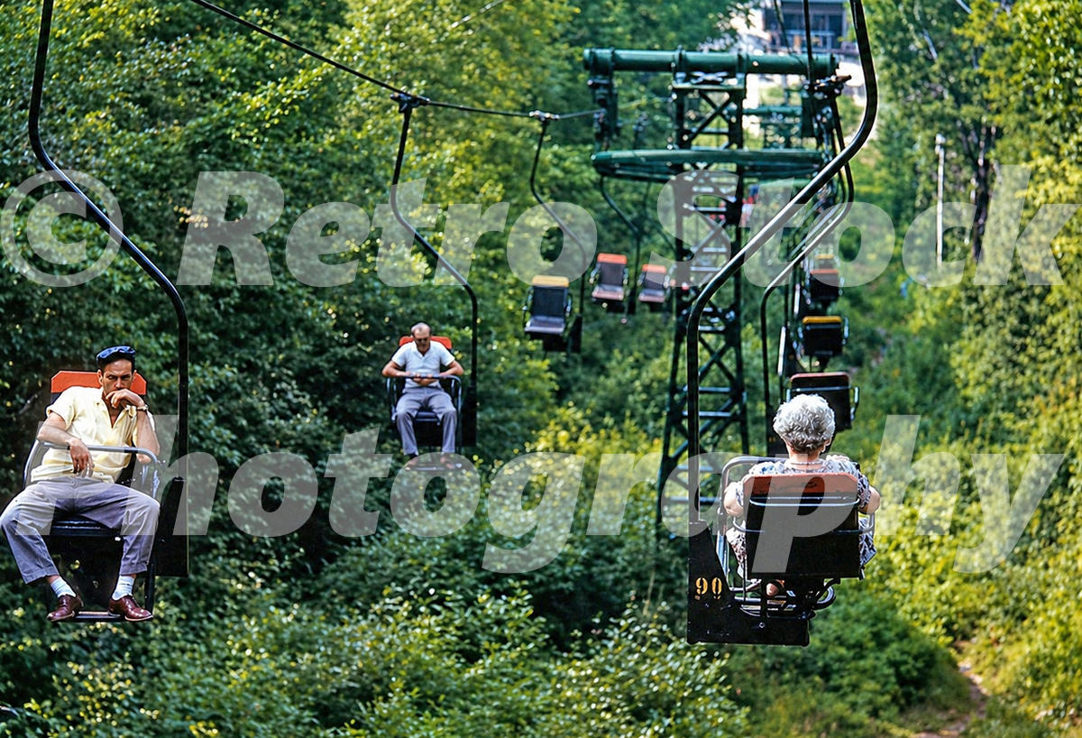 Genuine colour 1950s photograph of the chairlift at Mount Sunapee in New Hampshire, with single-seat chairs carrying summer visitors above woodland.