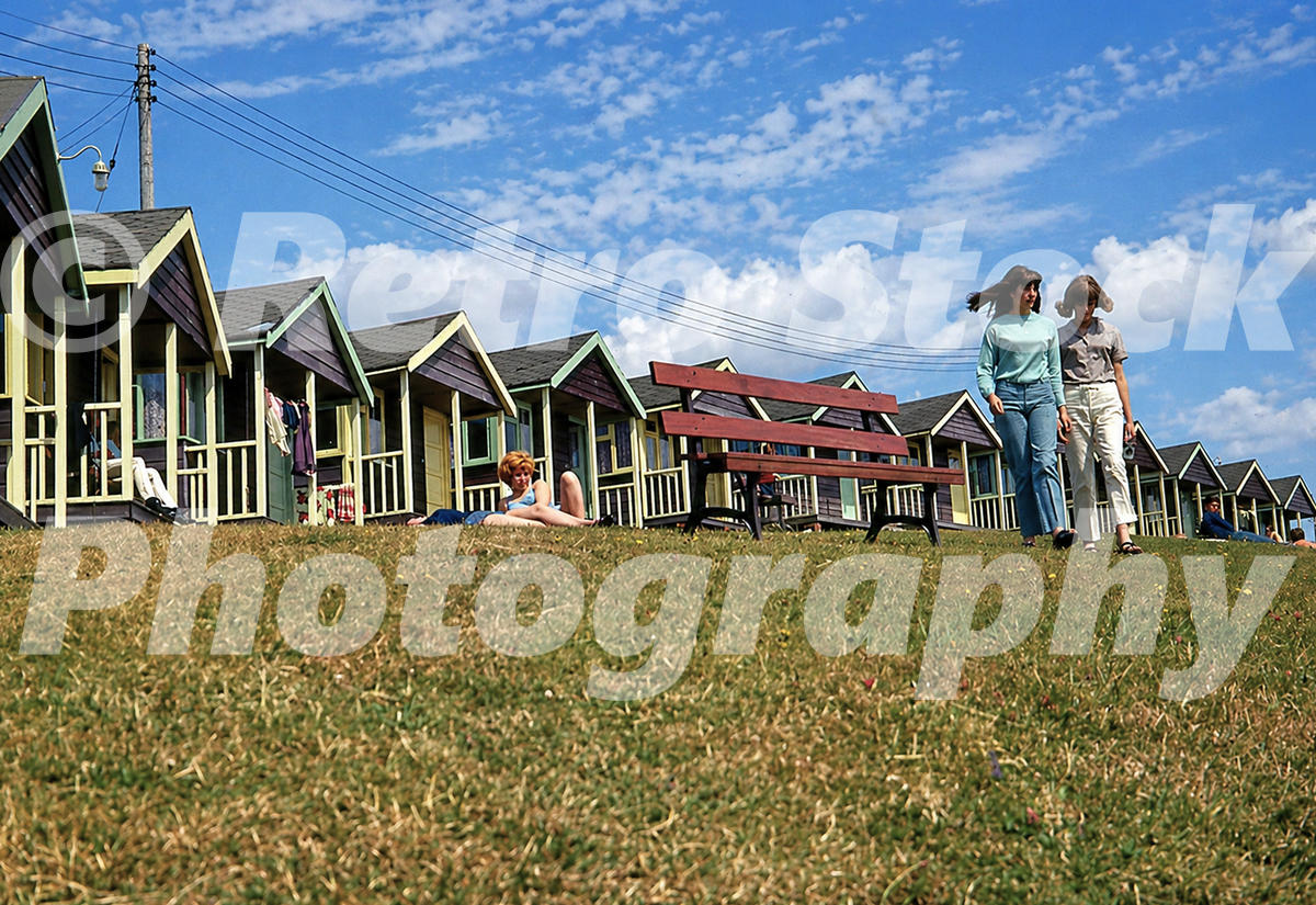 Pontins Osmington Bay Holiday Camp in the 1960s with rows of timber chalets, veranda fronts, bench seating and holidaymakers on the hillside