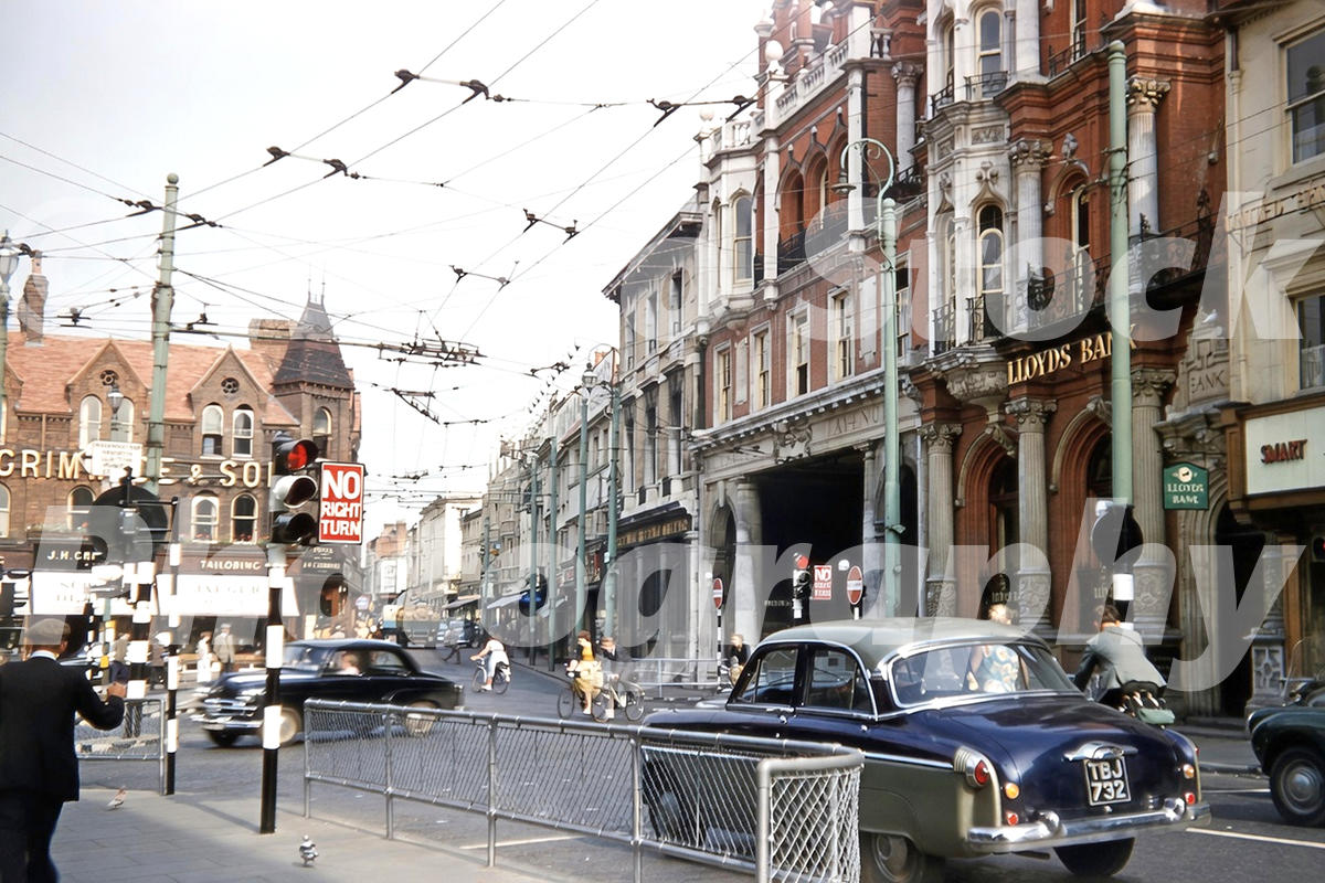 1950s view of Cornhill in Ipswich with Lloyds Bank, trolleybus wires, traffic lights, cyclists and cars.